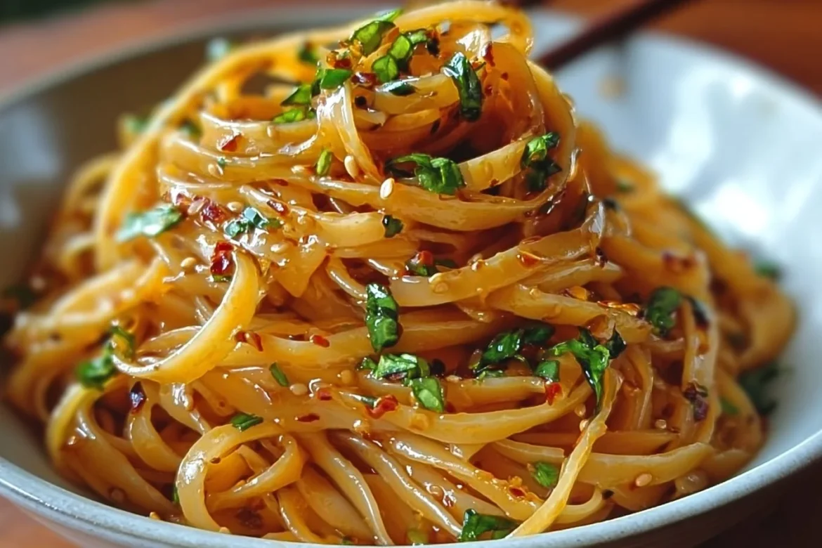 Bowl of Garlic Chili Oil Noodles garnished with fresh herbs and chili flakes