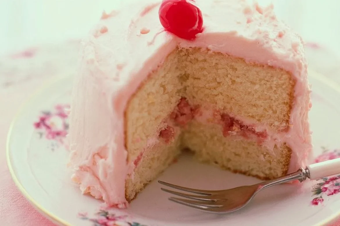 A slice of almond cake topped with maraschino cherry buttercream frosting