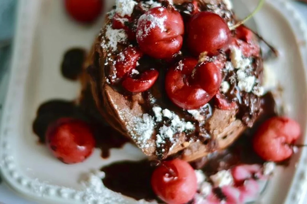Delicious Chocolate Cherry Pancakes stacked on a plate, garnished with cherries and chocolate syrup.