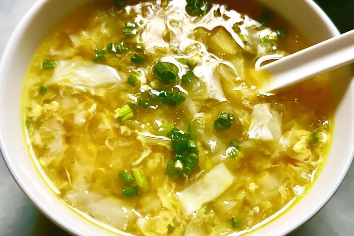 Bowl of cabbage egg drop soup garnished with green onions and sesame seeds.