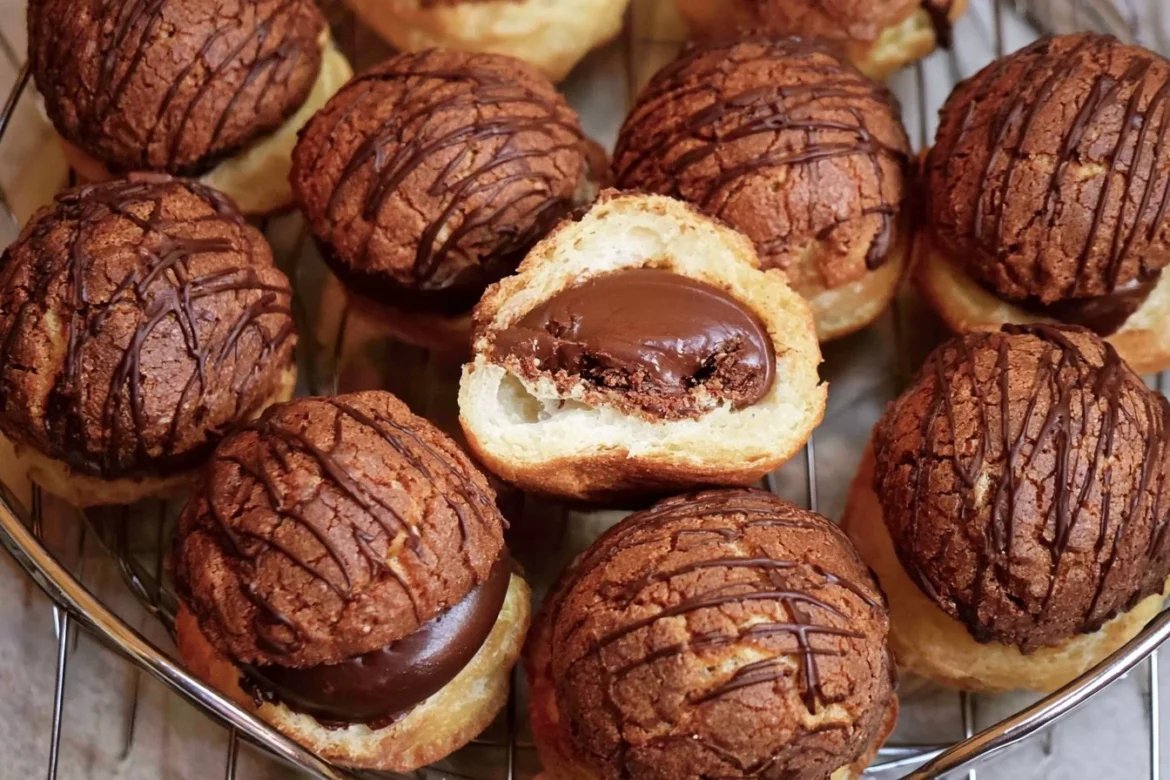 Delicious chocolate cream puffs topped with chocolate drizzle and powdered sugar.